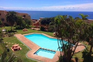 En pool med udsigt over havet, omgivet af palmer og en bygning.