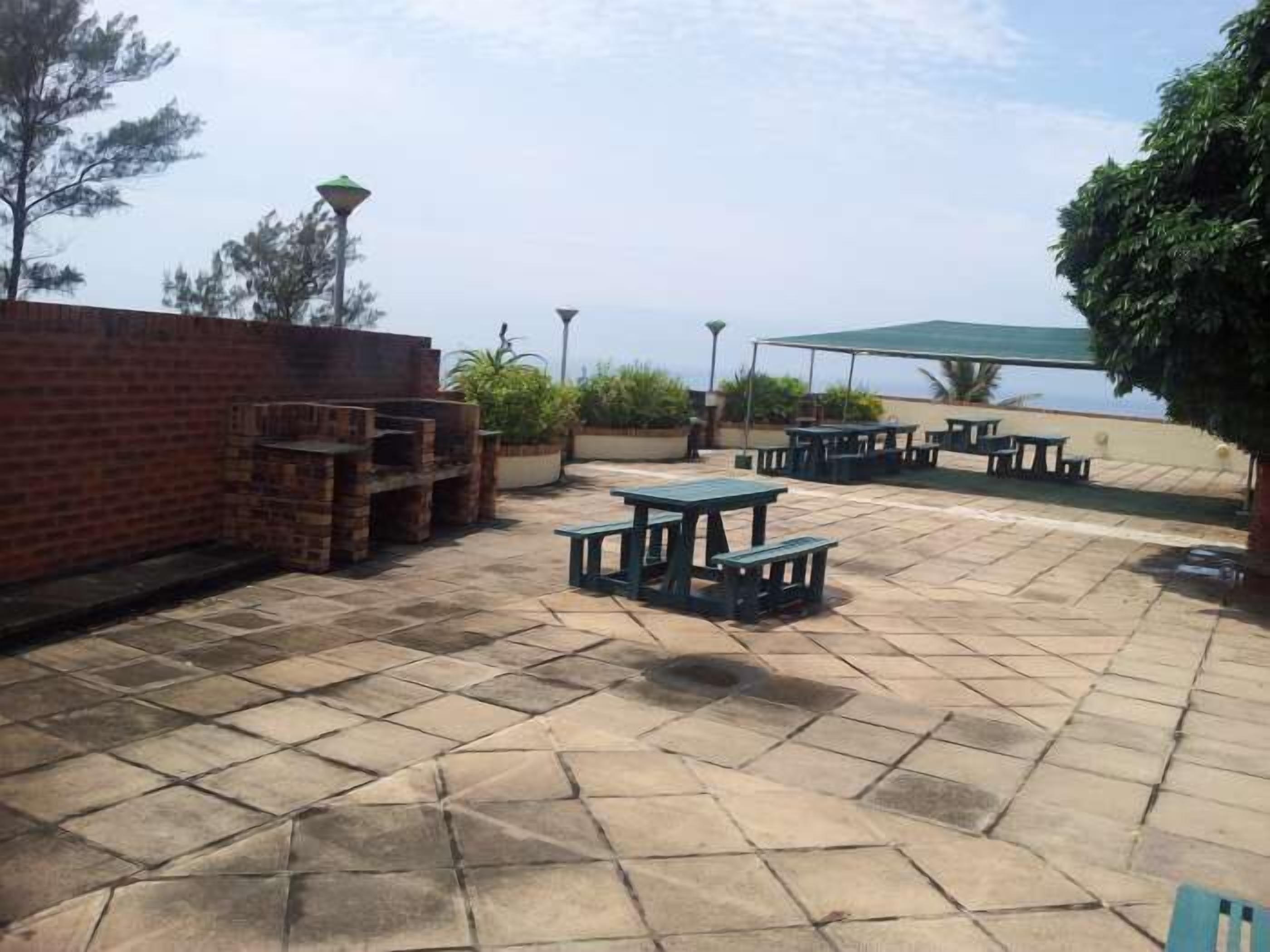 Une terrasse extérieure avec un sol en pierre, des tables de pique-nique et un mur en briques.