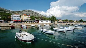 A marina with several boats docked, a stone wall, and buildings with balconies and shops. - Apartment in Starigrad near the Sea (Starigrad Paklenica)