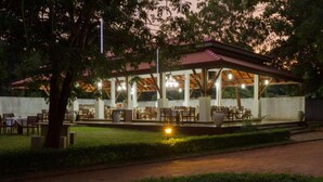 An outdoor dining area with tables and chairs, a covered pavilion, and a well-maintained garden. - Chenra Hotel (Kataragama)