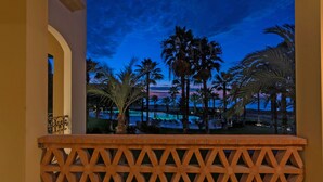 A balcony with a view of a pool area at dusk, featuring palm trees and a clear sky. - Paraiso Del Mar Resort PDM B203 1 Bedroom Condo by Seaside La Paz (La Paz)