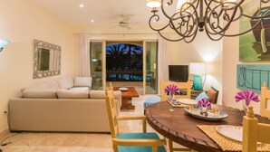 A living room with a sofa, dining table, and chairs. There is a TV on a stand and a painting on the wall. - Paraiso Del Mar Resort PDM B203 1 Bedroom Condo by Seaside La Paz (La Paz)