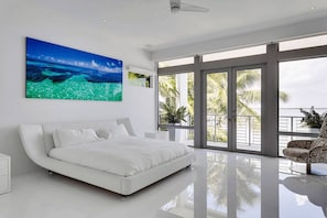 A modern bedroom with a large bed, a ceiling fan, and a view of the ocean through large windows. - Villa Venetian Star (Miami Beach)
