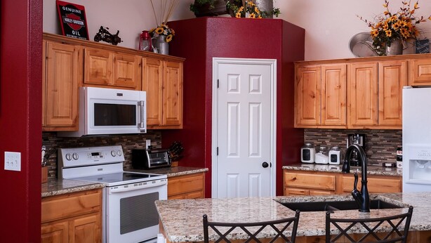A kitchen with wooden cabinets, a white door, a granite countertop, and various appliances including a microwave, stove, and toaster. - Gateway to Zion (La Verkin)
