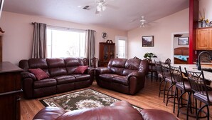 A living room with two leather sofas, a dining area with wooden chairs, and a kitchen with wooden cabinets. - Gateway to Zion (La Verkin)