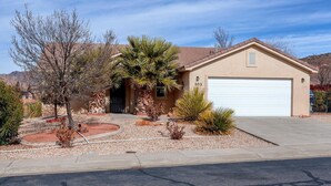 A single-story house with a garage, surrounded by landscaped gardens and desert vegetation. - Gateway to Zion (La Verkin)