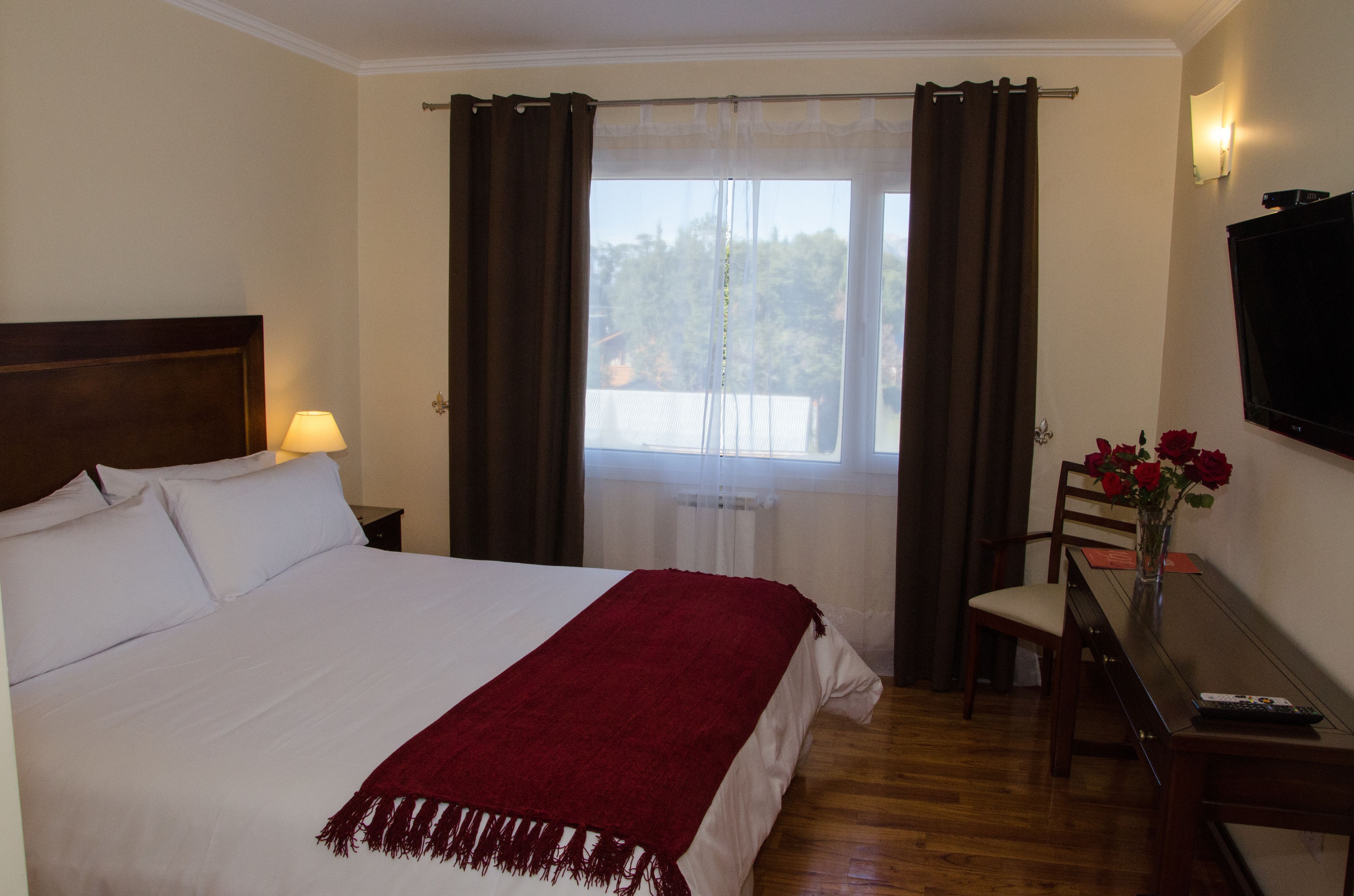 A hotel room with a large bed, a desk with a chair, a TV, and a window with curtains.