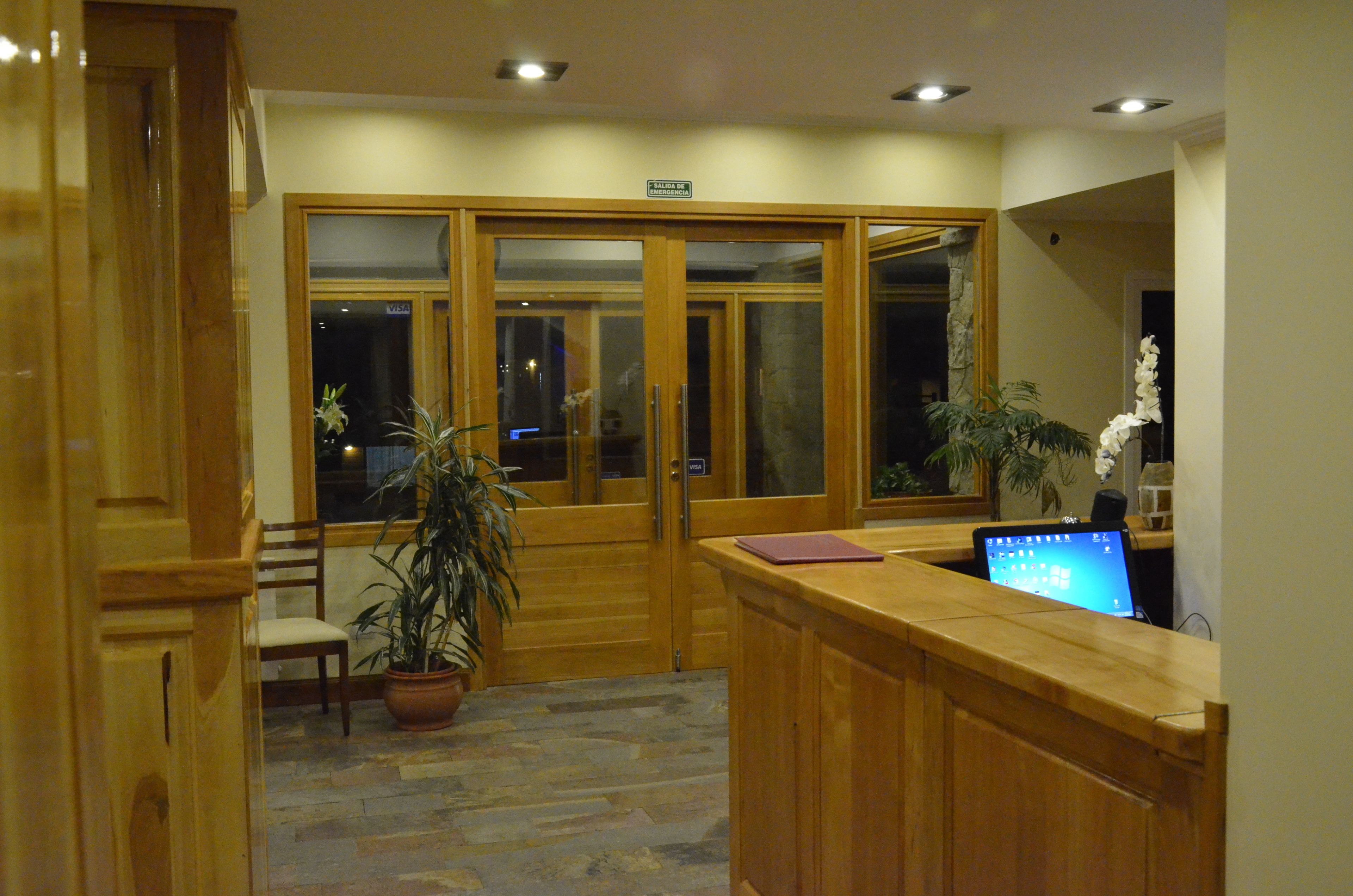 A reception area with a wooden desk, a computer, a chair, and potted plants.