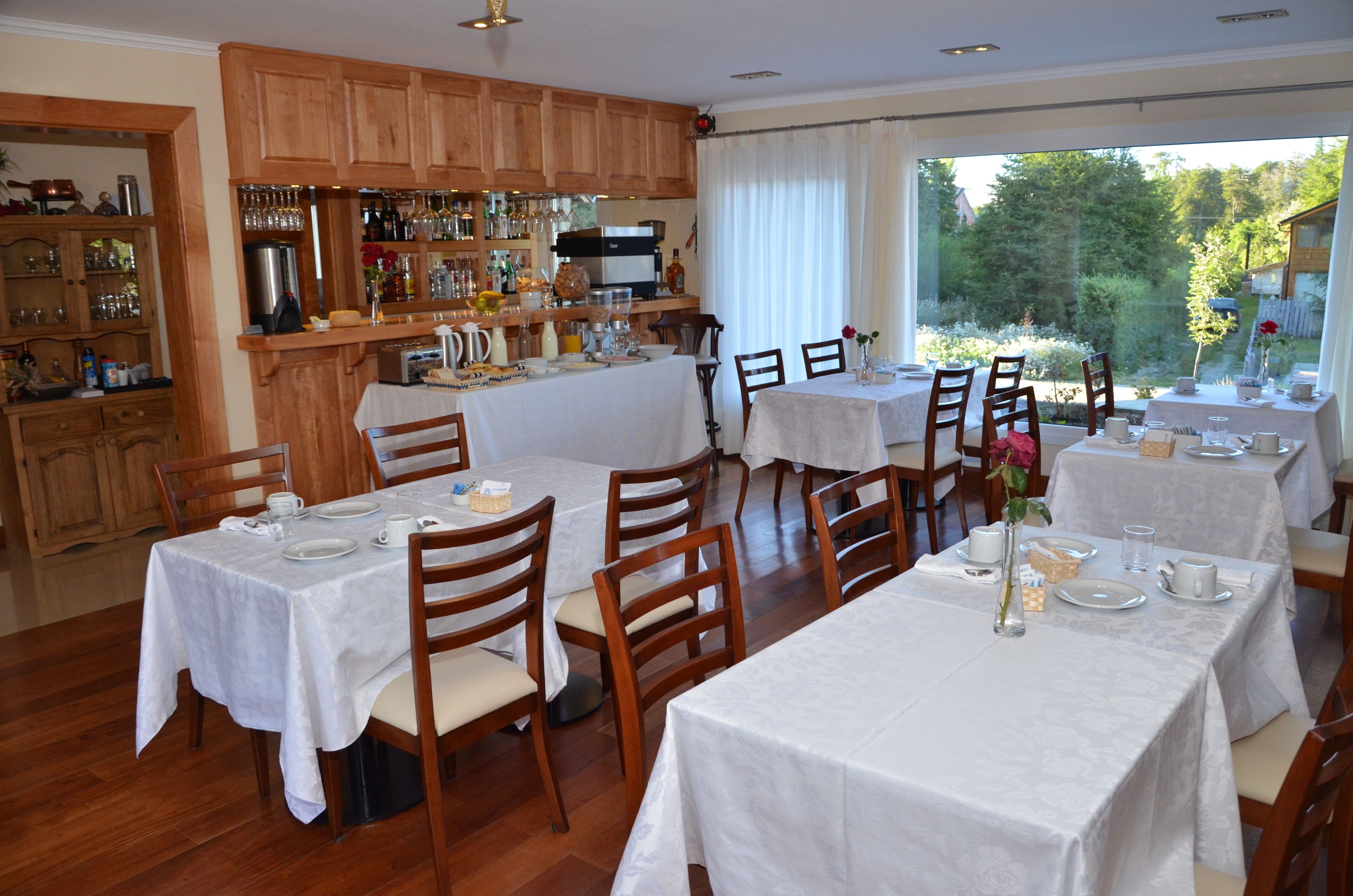 Un espace repas avec plusieurs tables dressées pour les repas, des meubles de rangement en bois et un bar avec diverses bouteilles et verres.