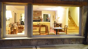 A stone-framed window with a view of a dining area, a sofa, and a staircase. - Alma Andina Hosteria (Villa La Angostura)