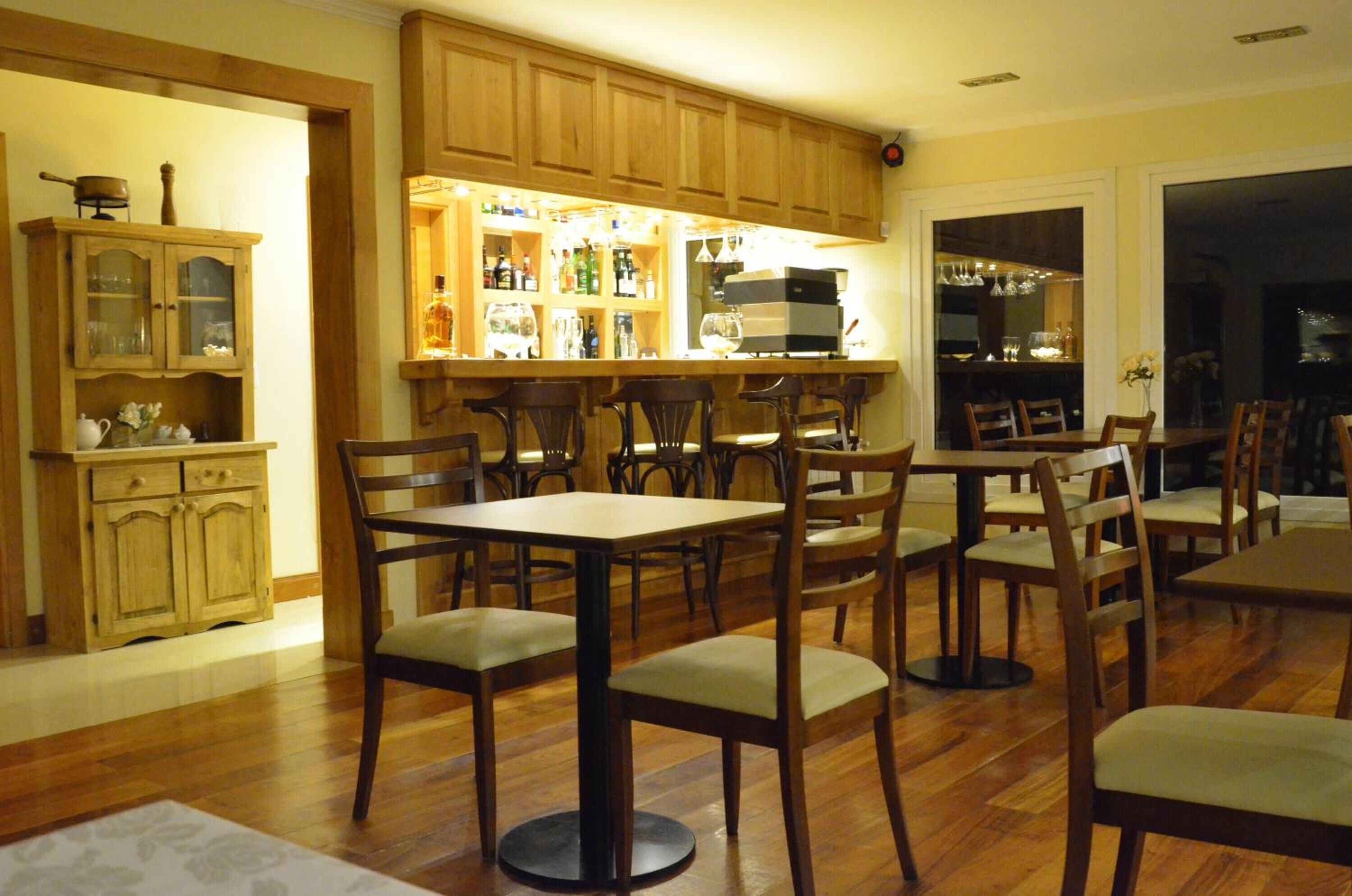 A dining area with wooden tables and chairs, a bar with shelves of bottles, and a kitchen area with wooden cabinets.