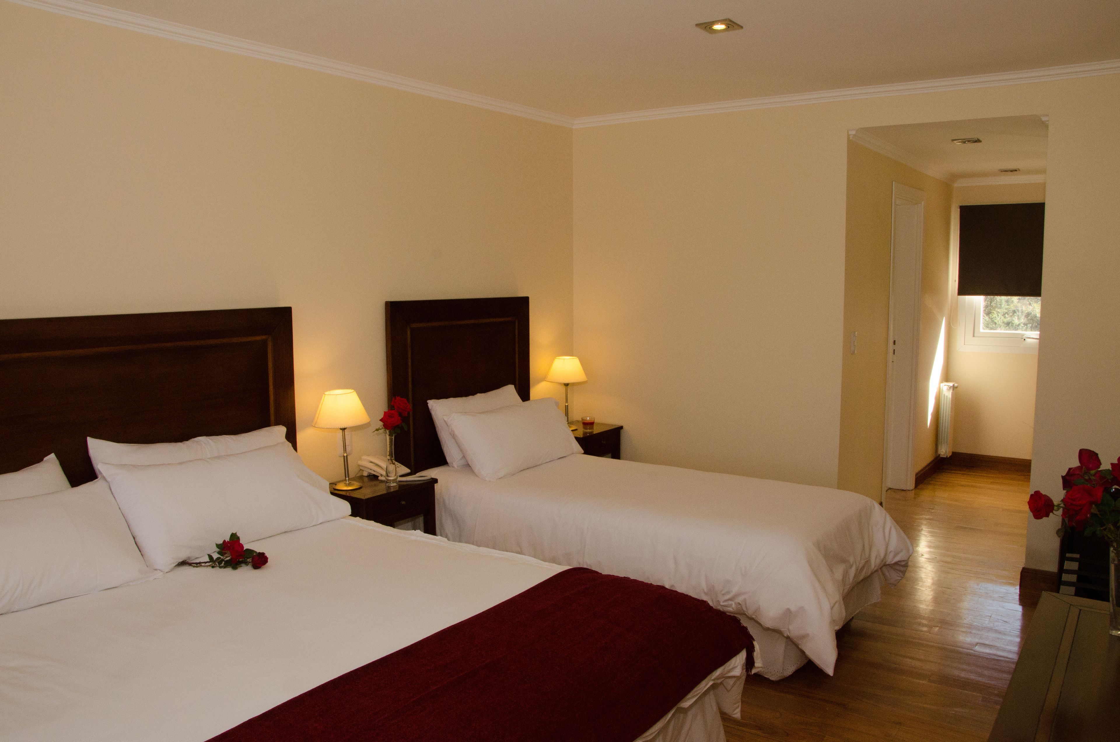 Hotelkamer met twee bedden, elk voorzien van een houten hoofdbord, wit beddengoed en een rode plaids. Op de nachtkastjes staan bedlampen met rode rozen.