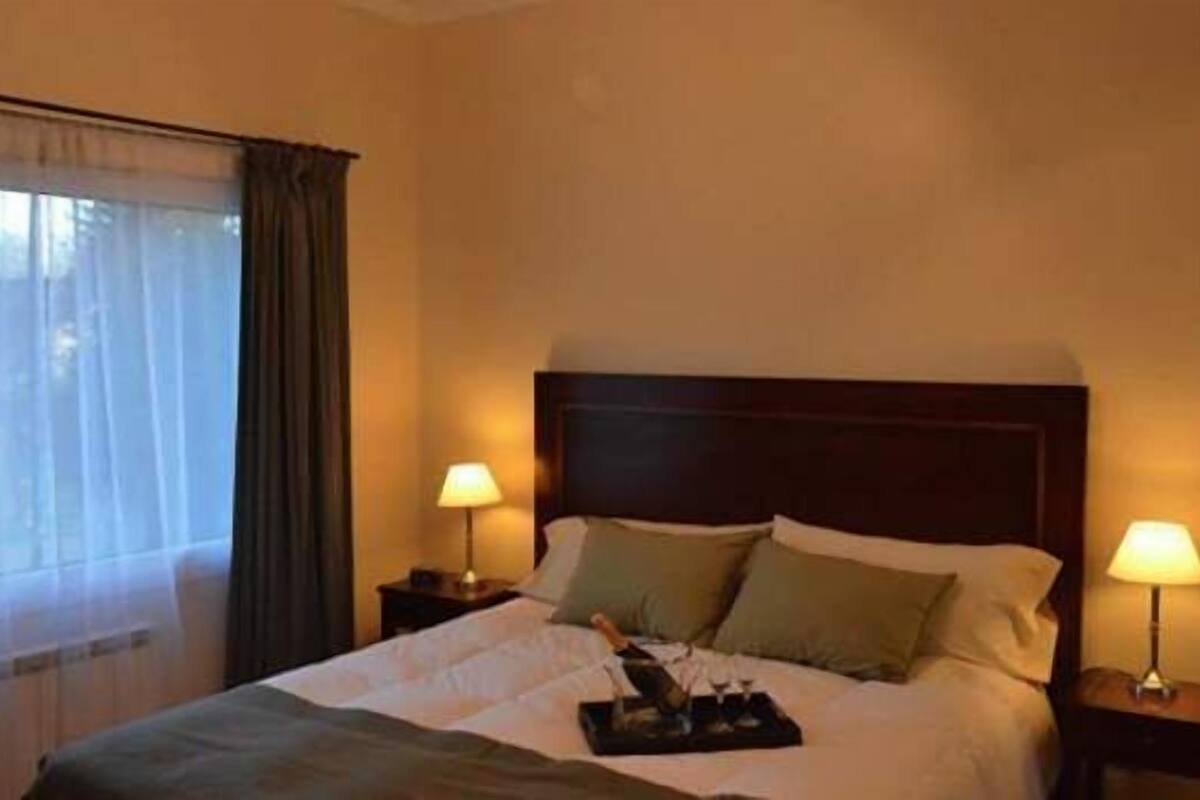 A hotel room with a bed, two bedside lamps, a window with curtains, and a bedside table with a tray.