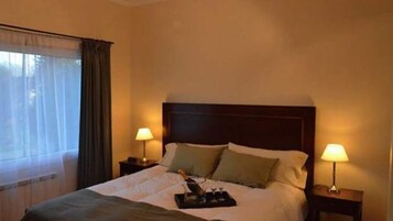 A hotel room with a bed, two bedside lamps, a window with curtains, and a bedside table with a tray.