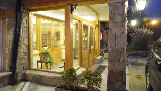 A stone-framed building with large glass doors, a bench outside, and a car parked nearby. - Alma Andina Hosteria (Villa La Angostura)