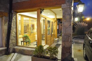 A stone-framed building with large glass doors, a bench outside, and a car parked nearby. - Alma Andina Hosteria (Villa La Angostura)