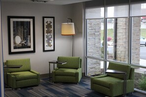 Une pièce comprenant trois fauteuils verts, un lampadaire et deux œuvres d’art encadrées accrochées au mur.