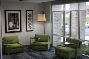 A room with three green armchairs, a floor lamp, and two framed artworks on the wall.