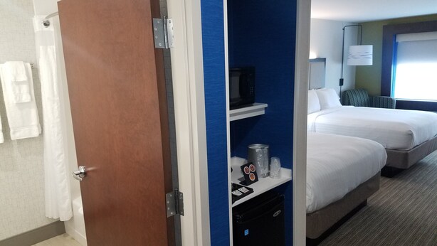 Una habitación de hotel con puerta de madera, baño con cortina de ducha y cama con mesita de noche.