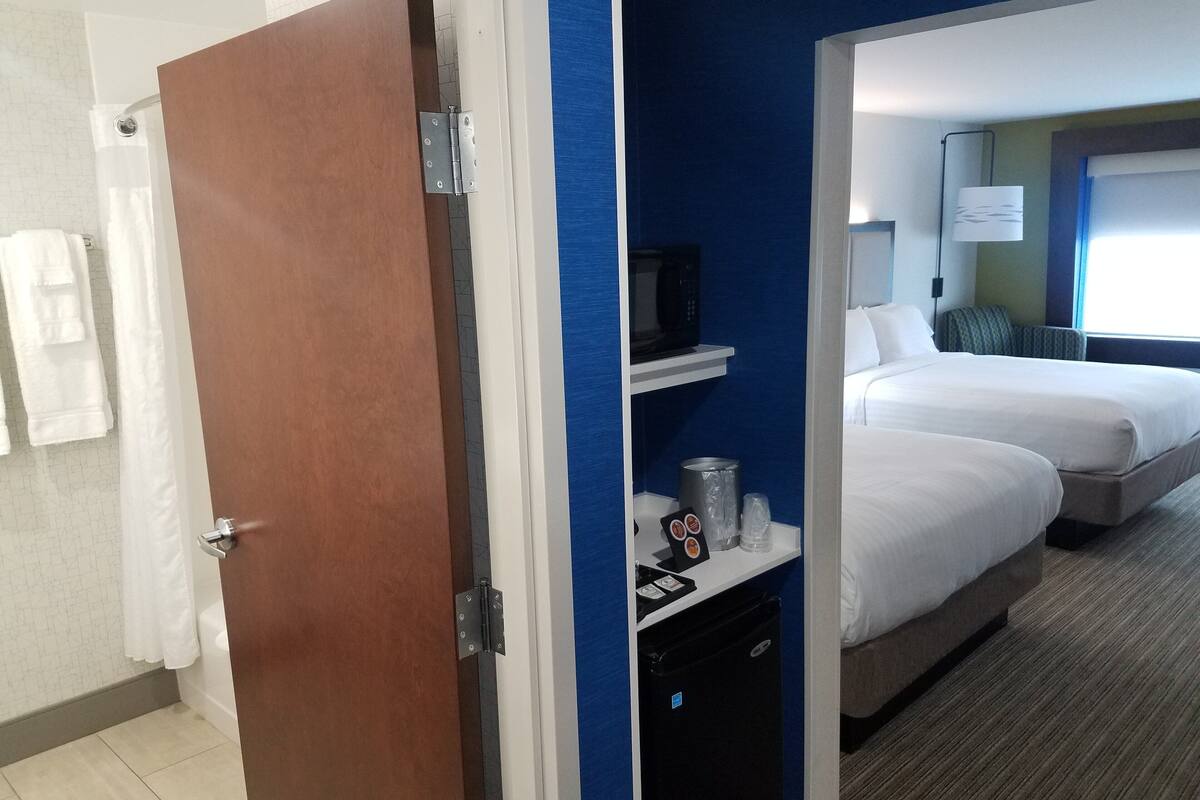 Una habitación de hotel con puerta de madera, baño con cortina de ducha y cama con mesita de noche.