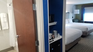 Une chambre d’hôtel avec une porte en bois, une salle de bain avec un rideau de douche et un lit avec une table de chevet.