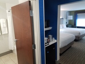 A hotel room with a wooden door, a bathroom with a shower curtain, and a bed with a bedside table.