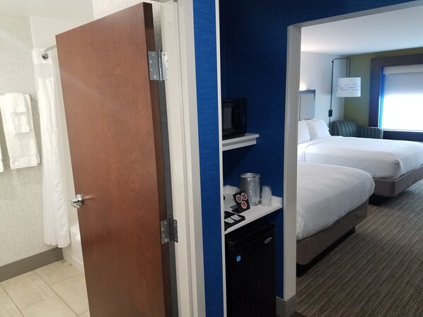 Una habitación de hotel con puerta de madera, baño con cortina de ducha y cama con mesita de noche.