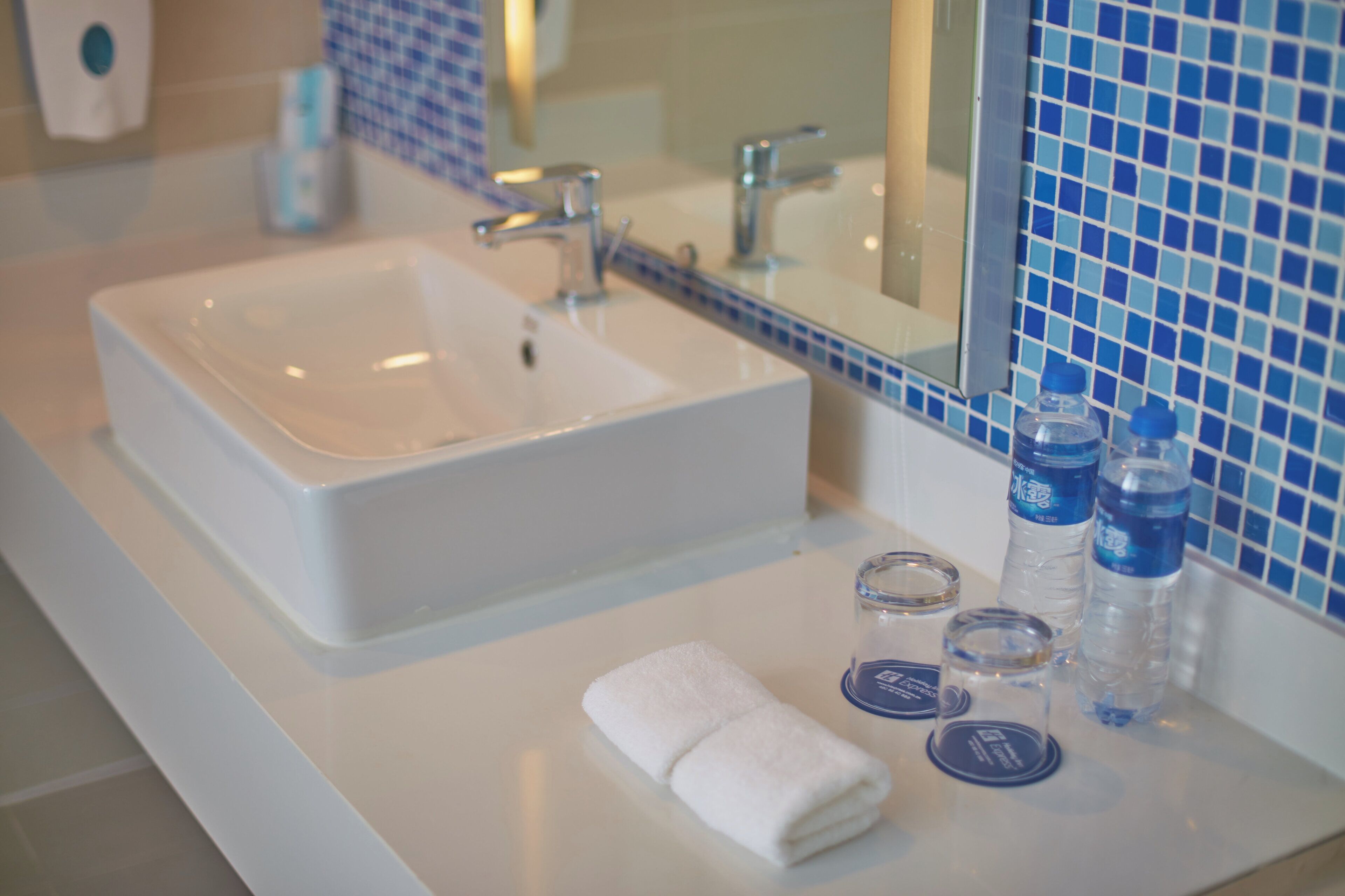A bathroom with a white sink, a mirror, and a blue tiled backsplash.