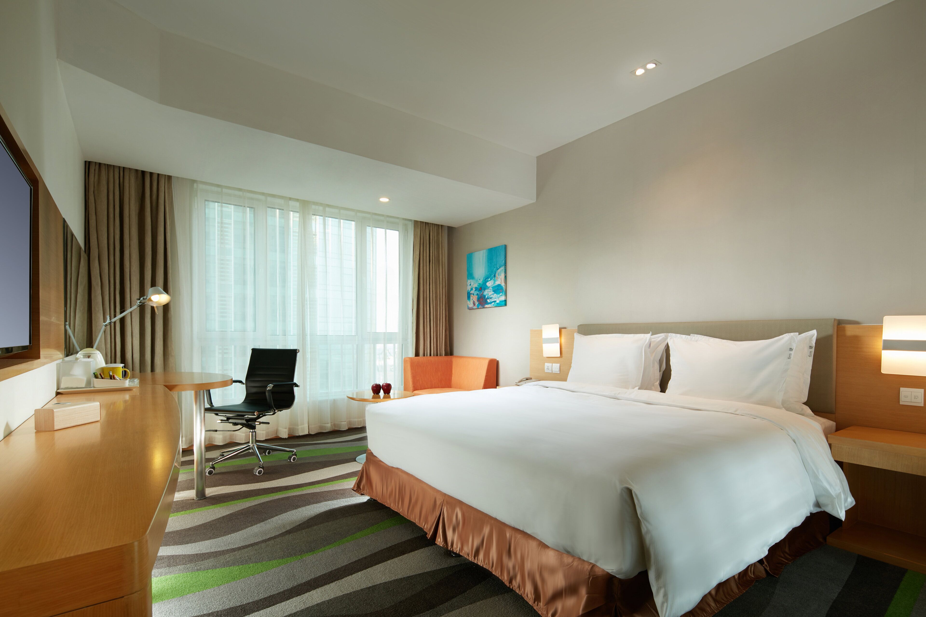 Una habitación de hotel con una cama grande, un escritorio, una silla, una mesita y una ventana con cortinas.