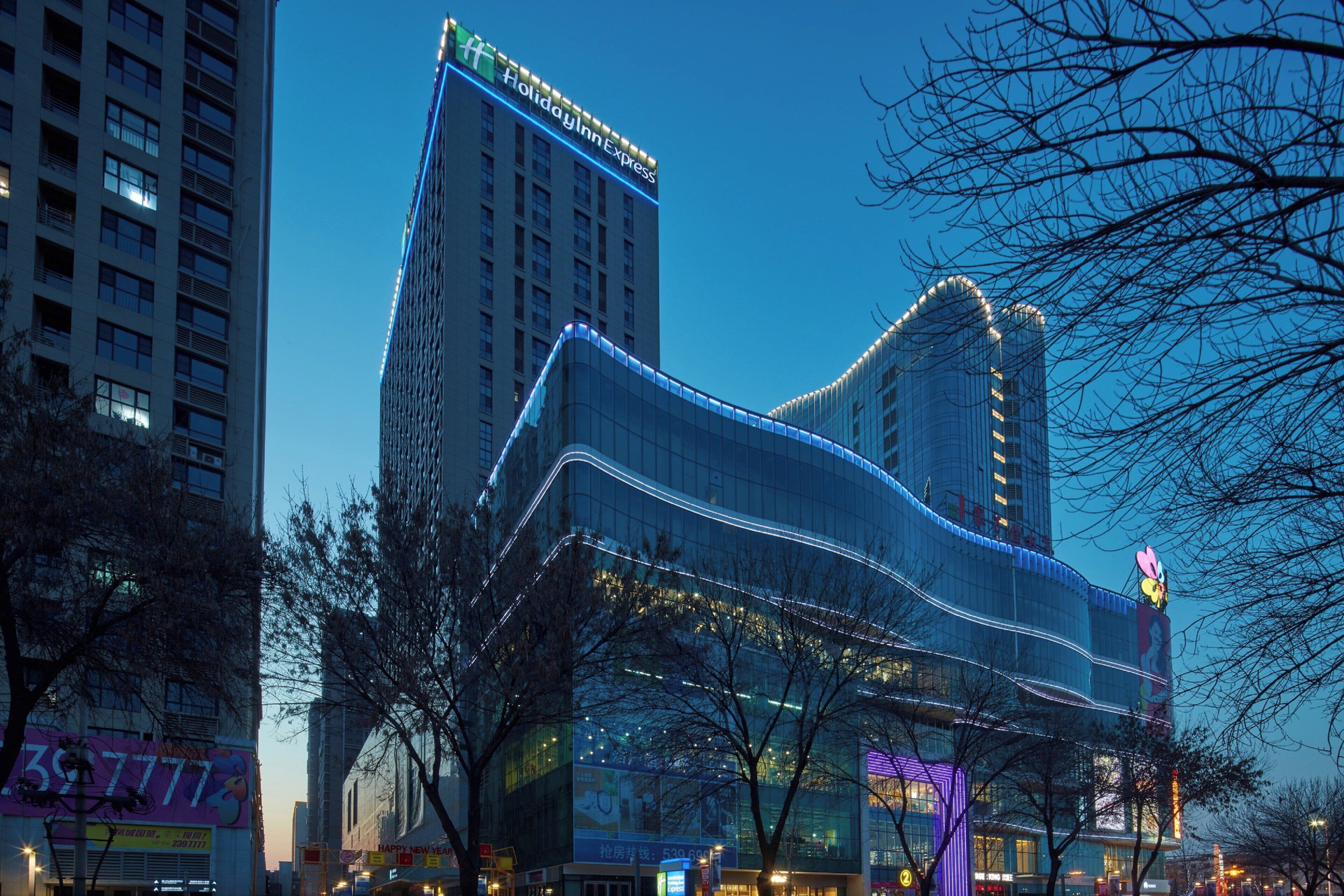 A modern hotel with a prominent Holiday Inn Express sign, surrounded by other buildings and trees.