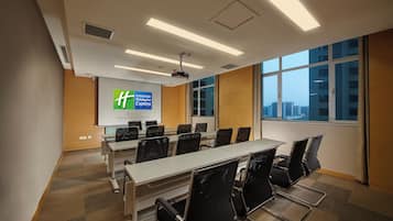 A conference room with a long table, chairs, a projector screen, and a view of the city through large windows.