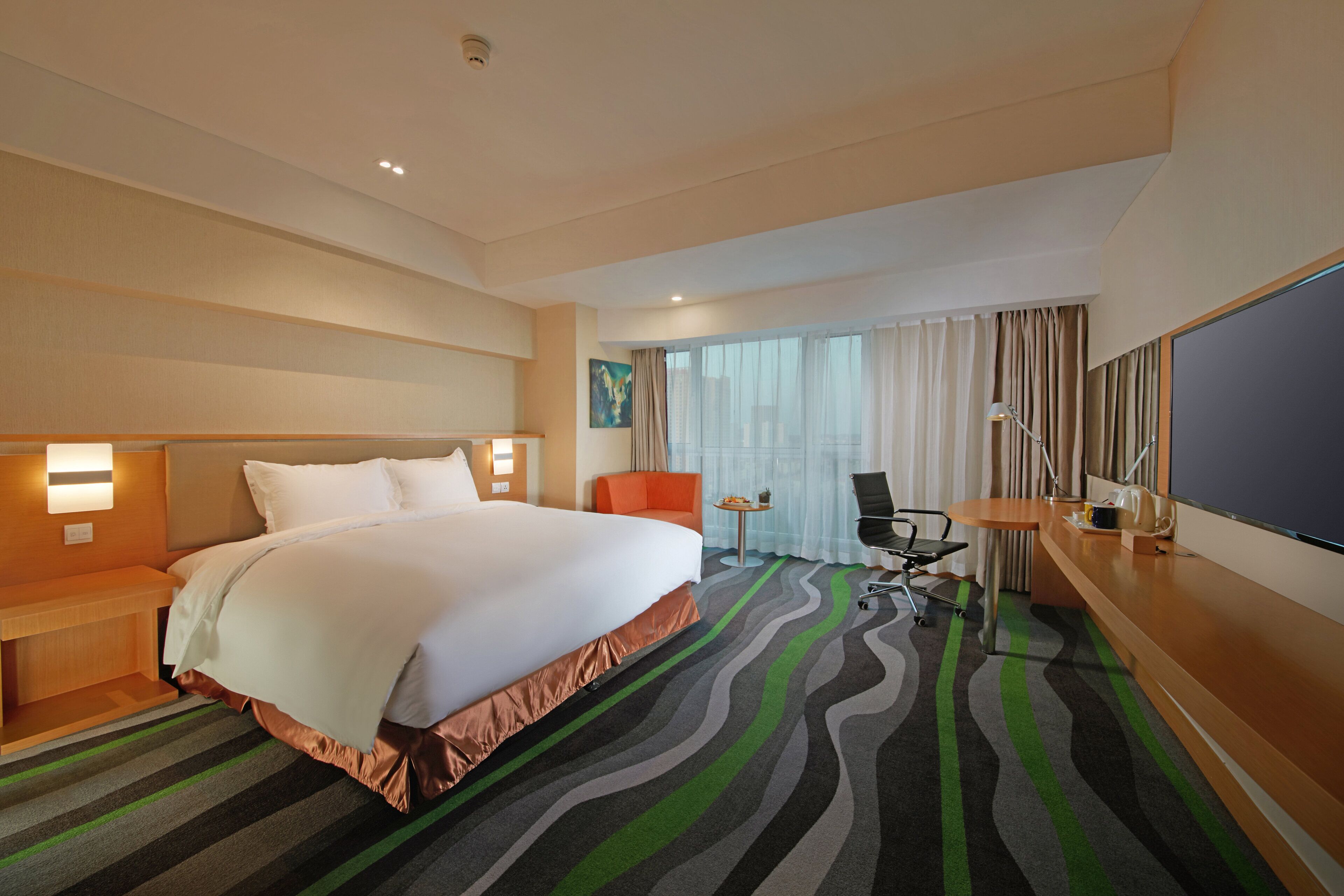 A hotel room with a large bed, a desk with a chair, a TV, and a window with curtains.