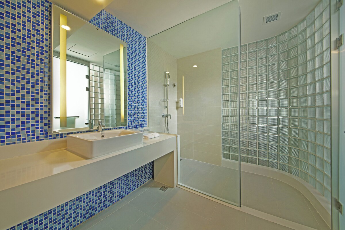 Een moderne badkamer met een glazen douchecabine, een grote spiegel en een wastafel met een blauwe betegelde spatwand.
