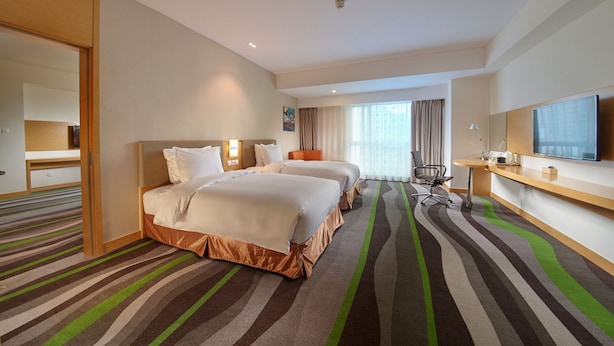 Quarto de hotel com duas camas, uma escrivaninha, uma cadeira, televisão e um espelho grande.