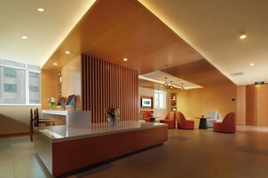 Un área de recepción moderna con un mostrador de madera, zona de estar y una pantalla de televisión.