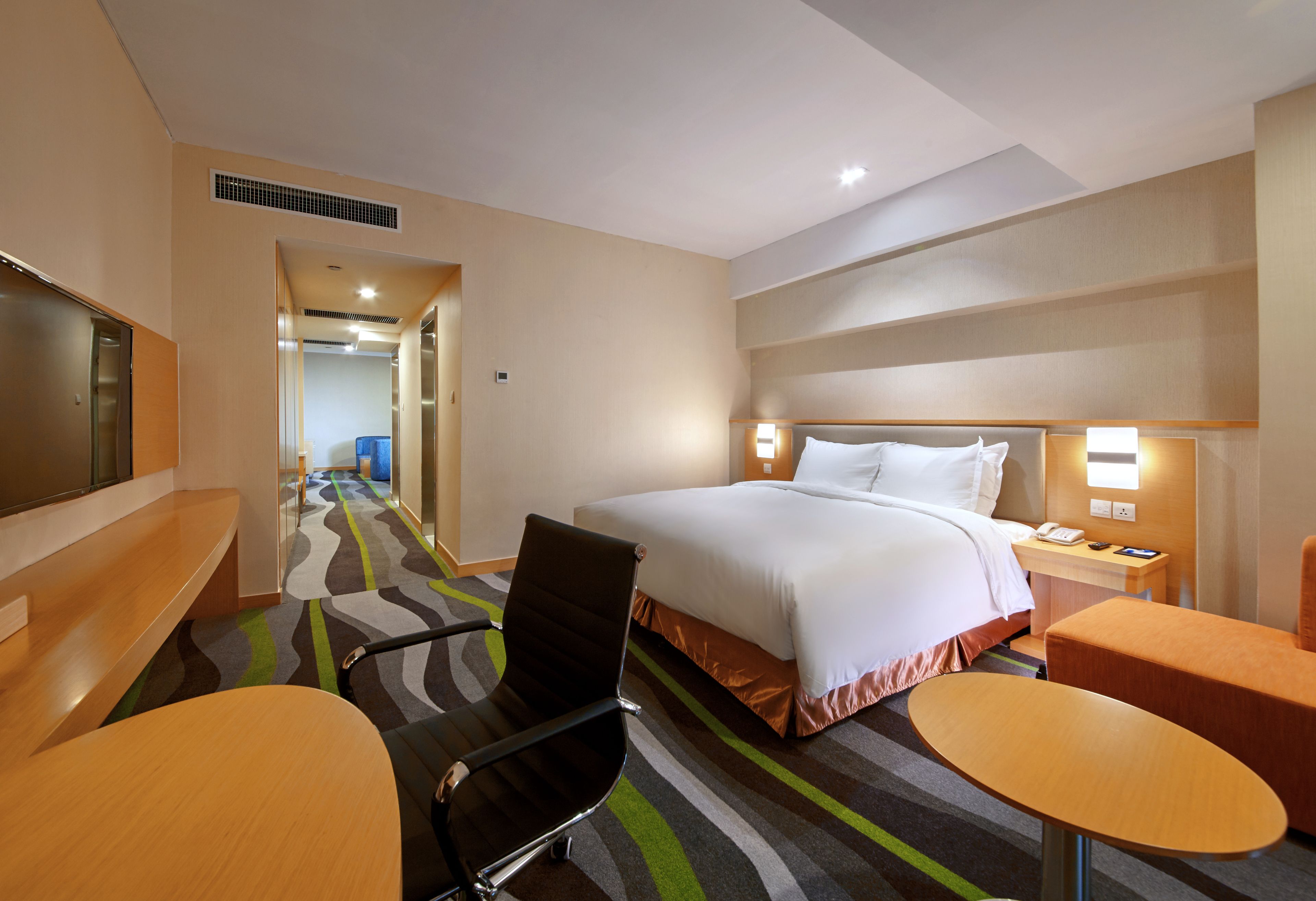A hotel room with a bed, a desk, a chair, and a small table.