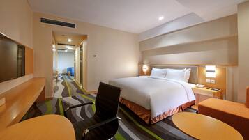 A hotel room with a bed, a desk, a chair, and a small table.