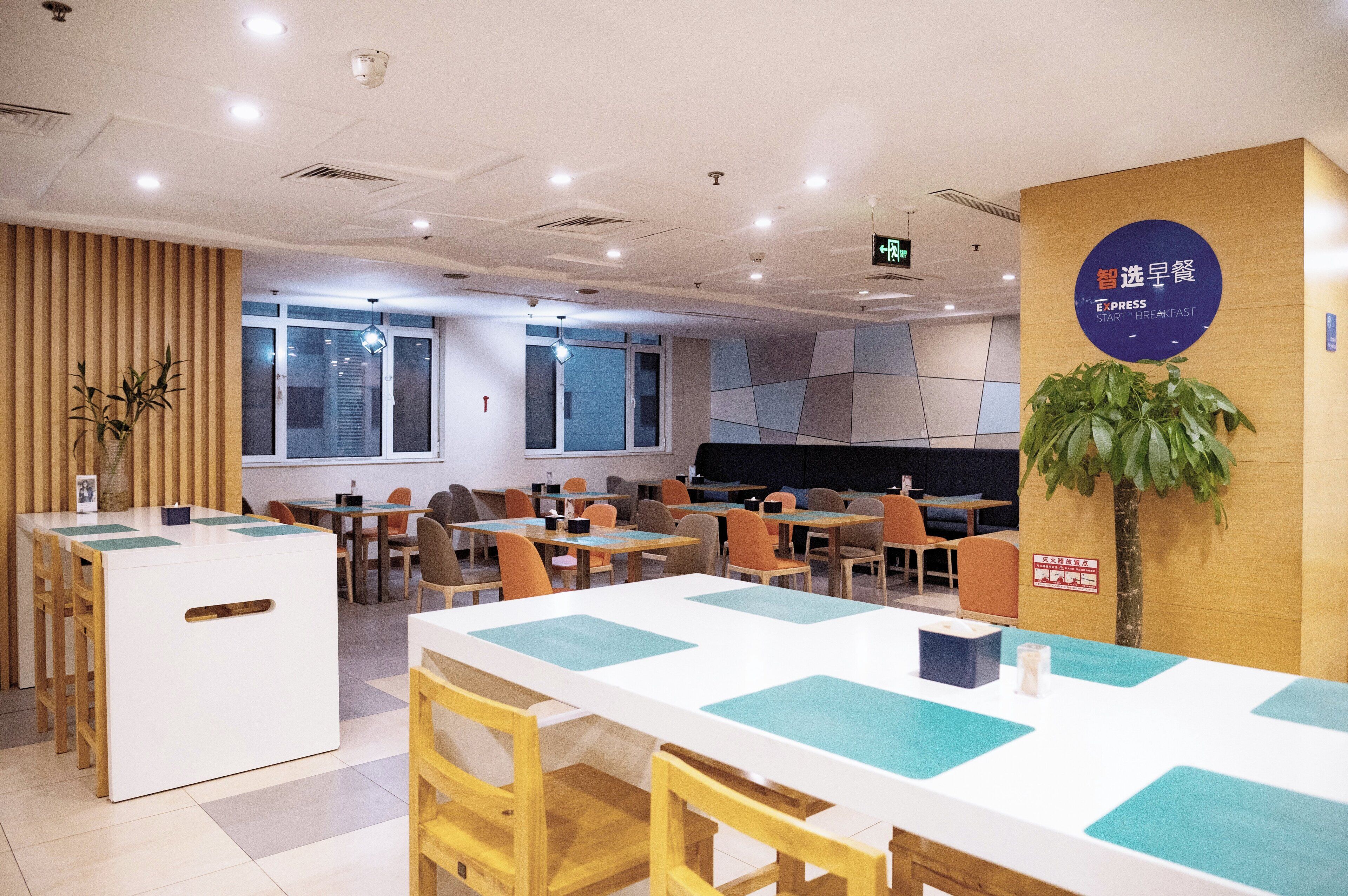 A modern dining area with tables and chairs, a reception desk, and a sign indicating breakfast service.