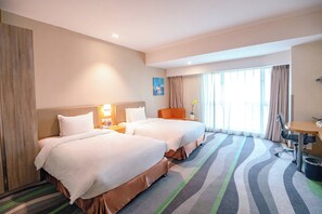 Een hotelkamer met twee bedden, een bureau, een stoel en een groot raam met gordijnen.