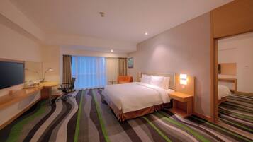 A hotel room with a bed, a desk, a chair, a television, and a window with curtains.