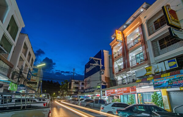 Une vue de rue au crépuscule, avec des bâtiments, des voitures et des enseignes illuminées.