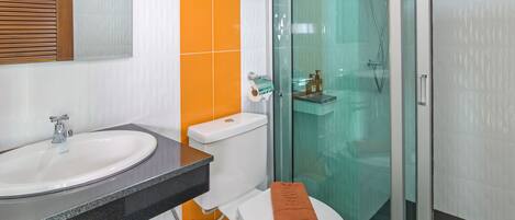 Baño con lavamanos blanco, inodoro y ducha con mampara de vidrio.