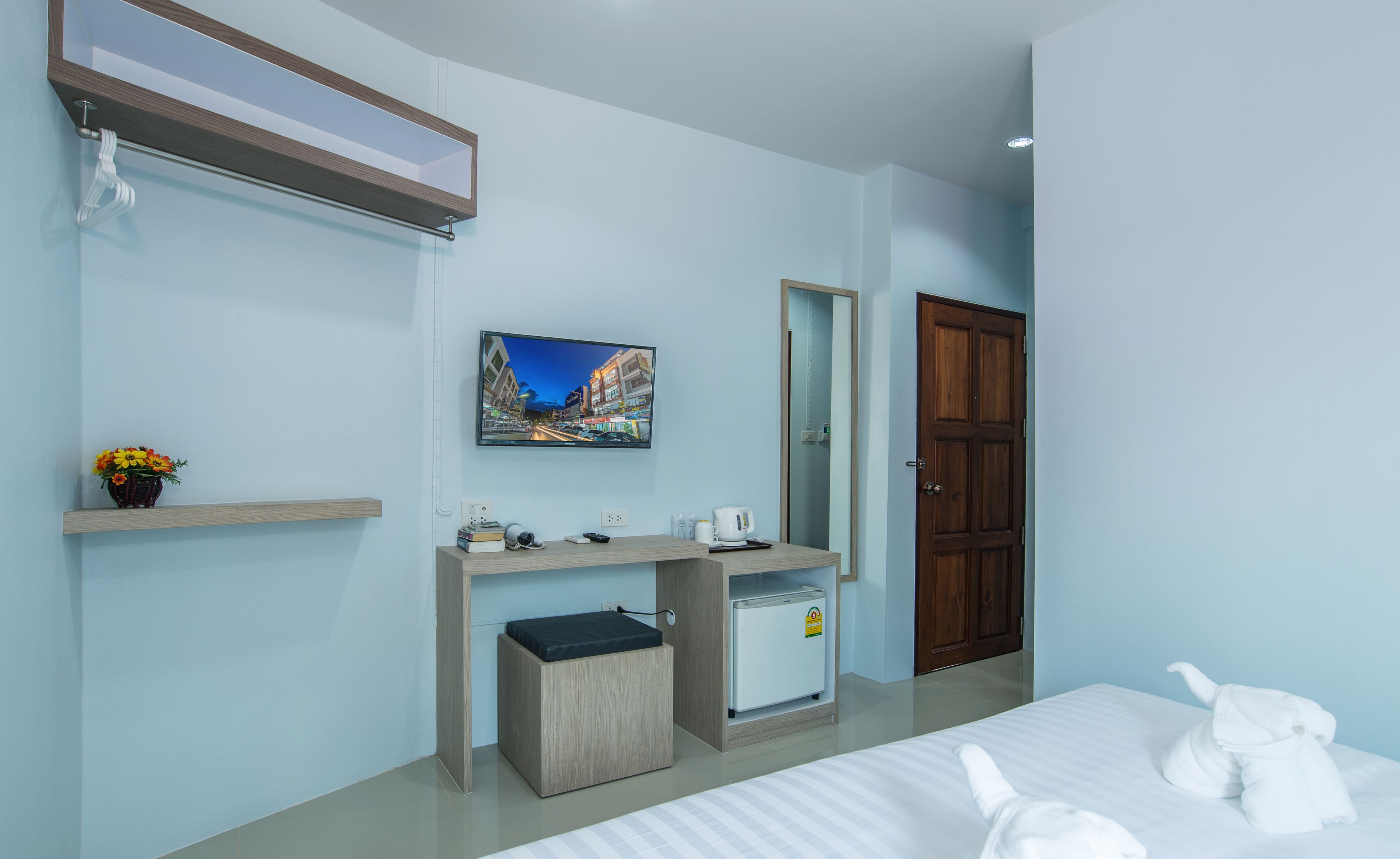 A hotel room with a bed, a small desk with a mirror, a television, and a door.