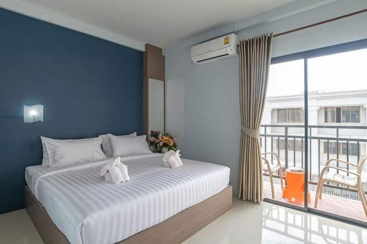 Habitación de hotel con una cama grande, un balcón con sillas y vistas a la ciudad.