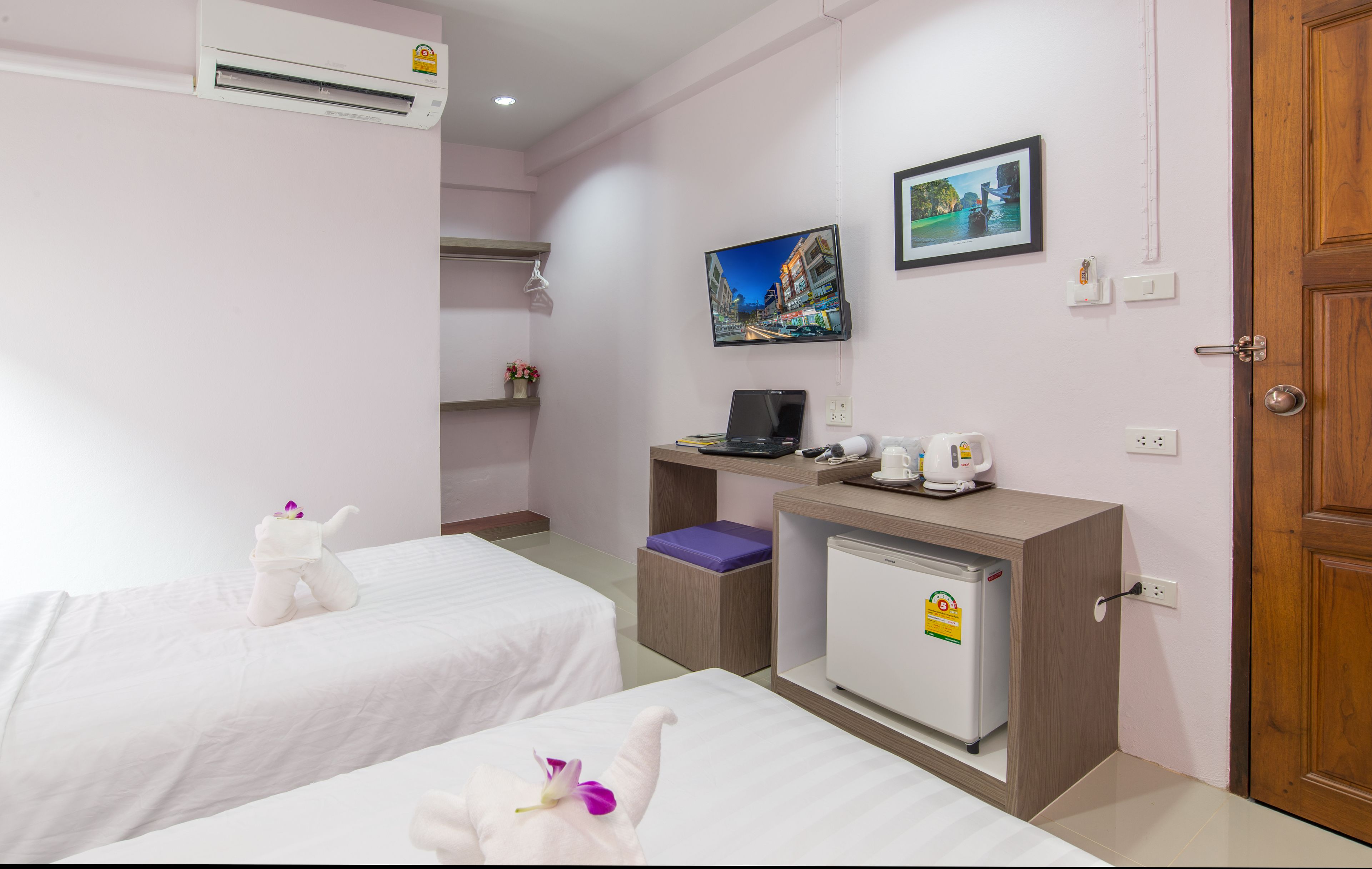 A hotel room with two beds, a desk with a laptop, a mini-fridge, and a television on the wall.