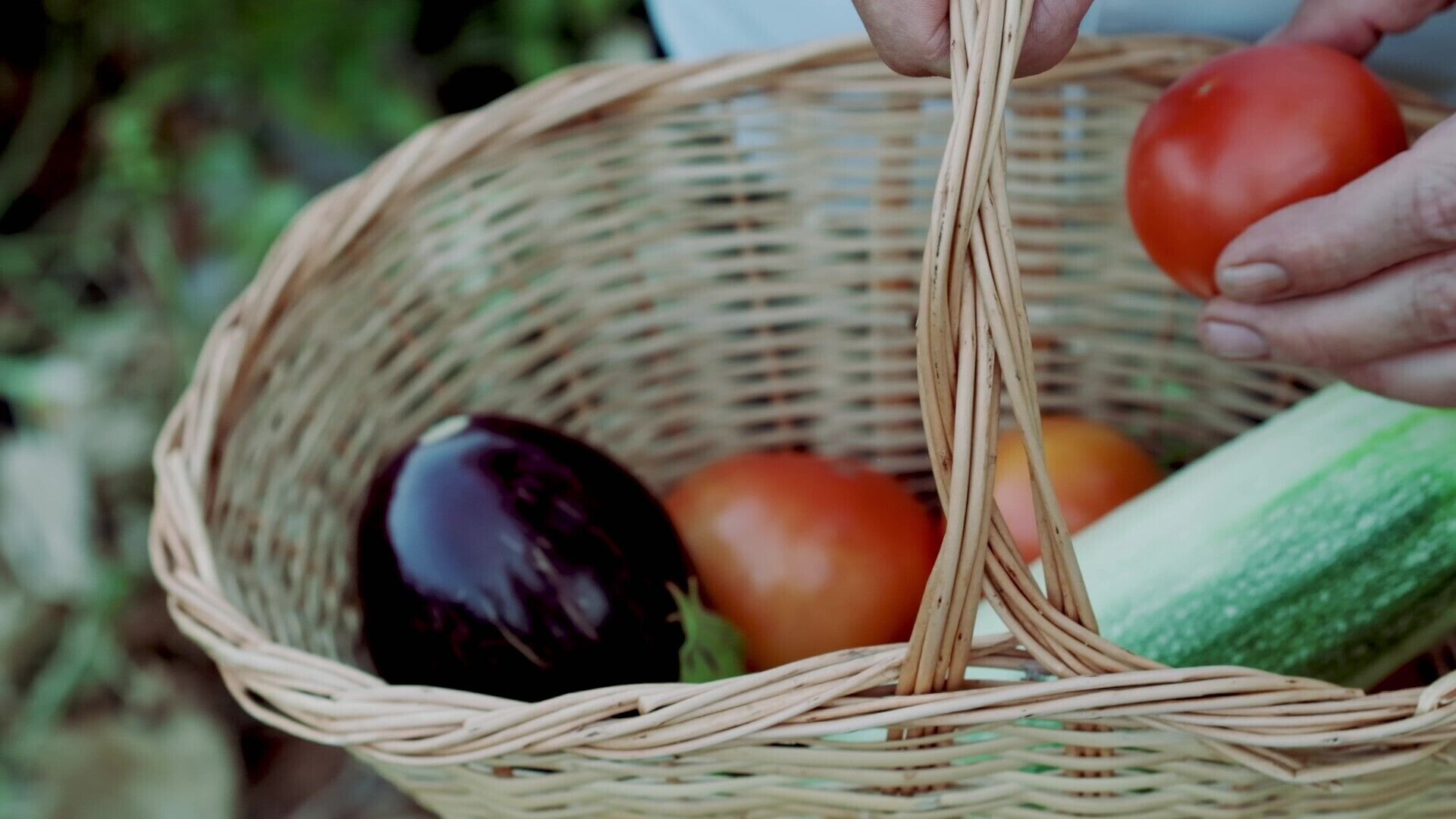 Una cesta de mimbre con un tomate, un pepino y una berenjena.