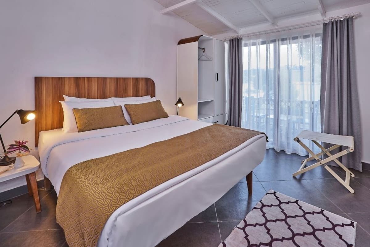 Une chambre d’hôtel bien aménagée, avec un grand lit, une table de chevet avec une lampe, une armoire et une fenêtre avec des rideaux.