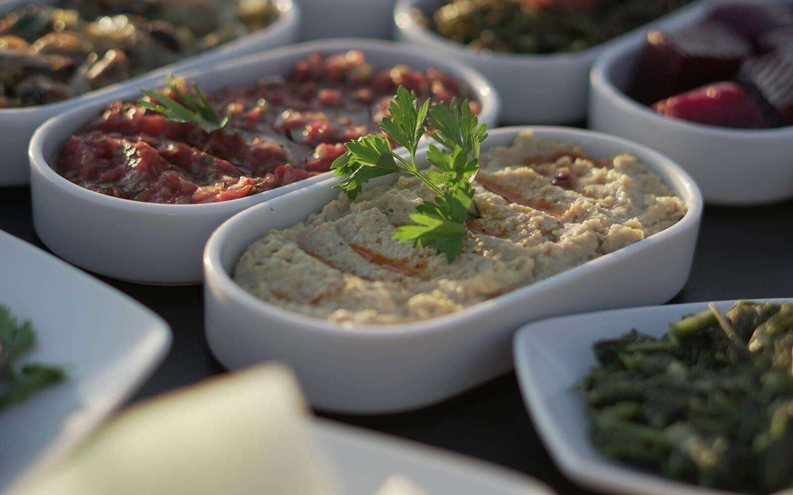 A variety of dishes in white bowls, including a hummus topped with parsley.