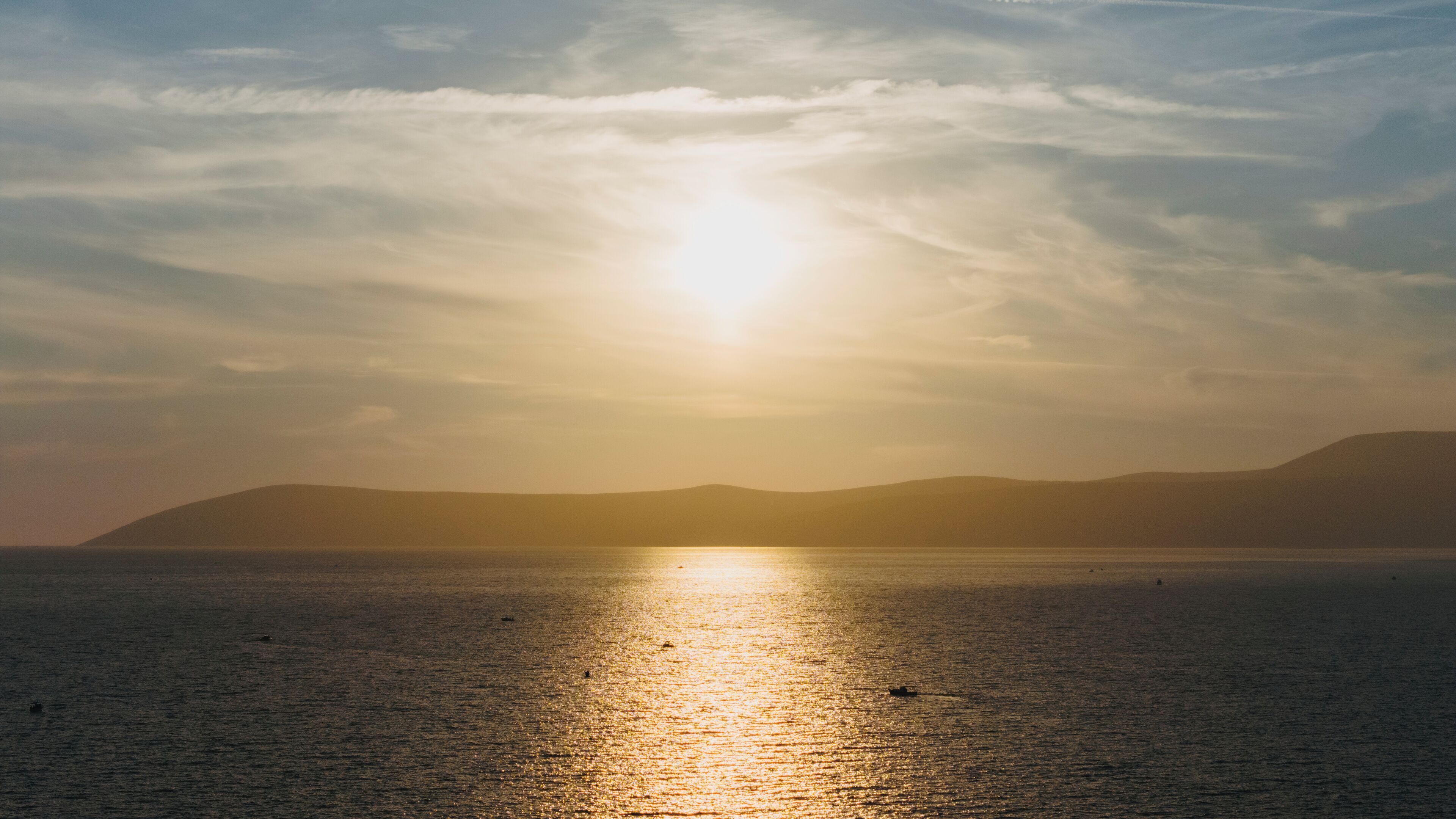 Un atardecer sobre un mar tranquilo con colinas a lo lejos.