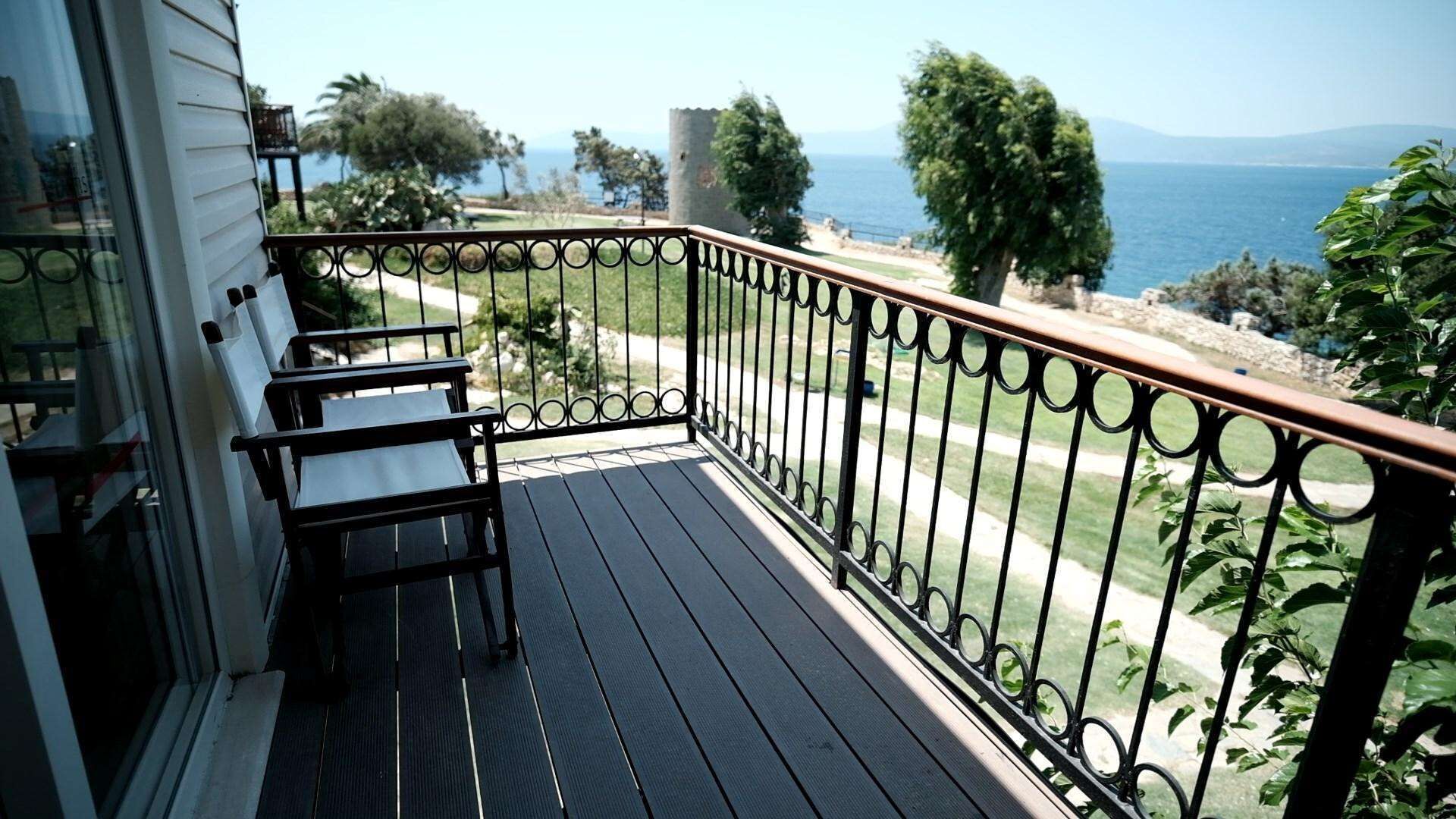 A balcony with a view of the sea, a stone tower, and a wooden deck.